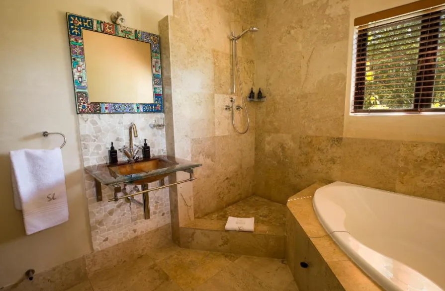 Stone tiled guest bathroom with a bath, shower and decorative mirror